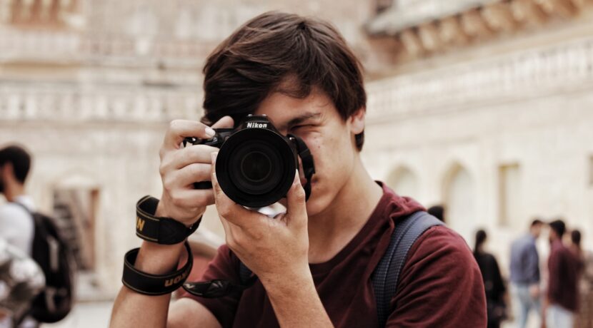 man in red and black crew neck t-shirt holding black nikon dslr camera