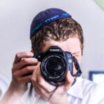 man in blue knit cap holding black and silver nikon dslr camera