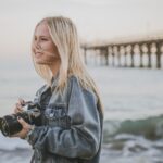 woman holding camera standing on seashore
