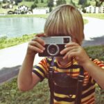 girl in yellow and black stripe shirt holding gray and black camera