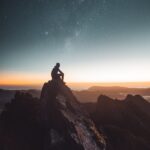 silhouette of person sitting on rock formation during golden hour