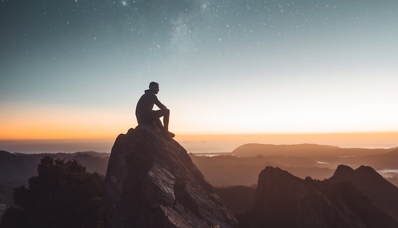 silhouette of person sitting on rock formation during golden hour