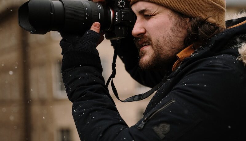 man in black jacket and brown knit cap holding black dslr camera