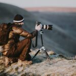 man taking photo using black and white DSLR camera on hill at daytime