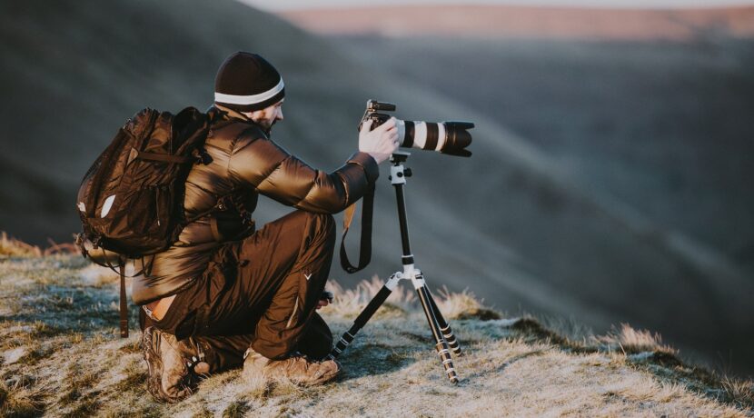 man taking photo using black and white DSLR camera on hill at daytime