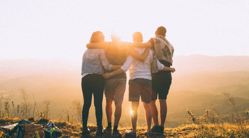 four person hands wrap around shoulders while looking at sunset