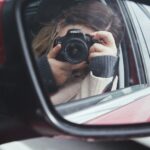 a woman taking a picture of herself in a car mirror