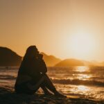 silhouette of woman sitting on beach during sunset