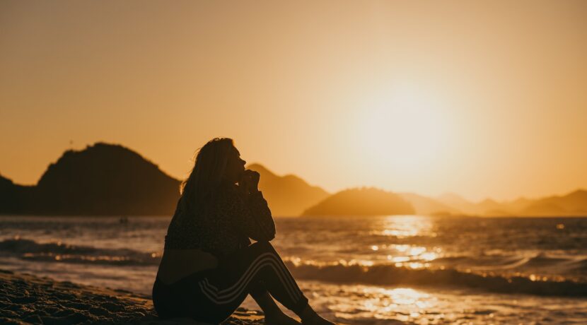 silhouette of woman sitting on beach during sunset
