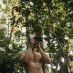 a shirtless man taking a selfie in the woods