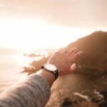 left person's arm wearing watch pointing body of water