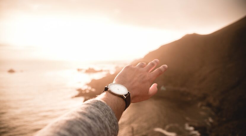 left person's arm wearing watch pointing body of water
