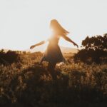 silhouette of woman dancing in the middle of grass field