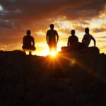 silhouette photography of four person on cliff during sunset