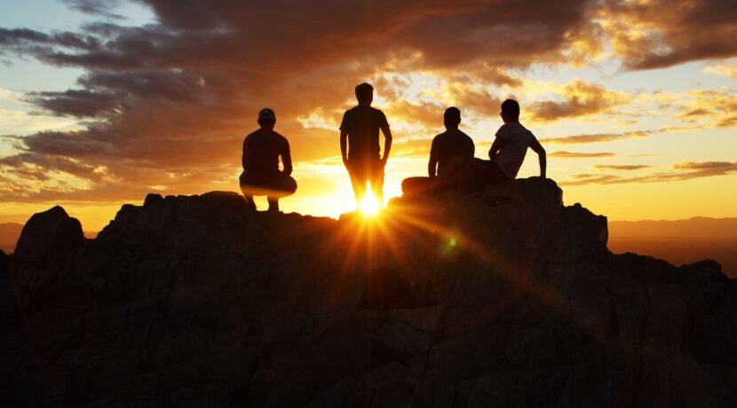 silhouette photography of four person on cliff during sunset