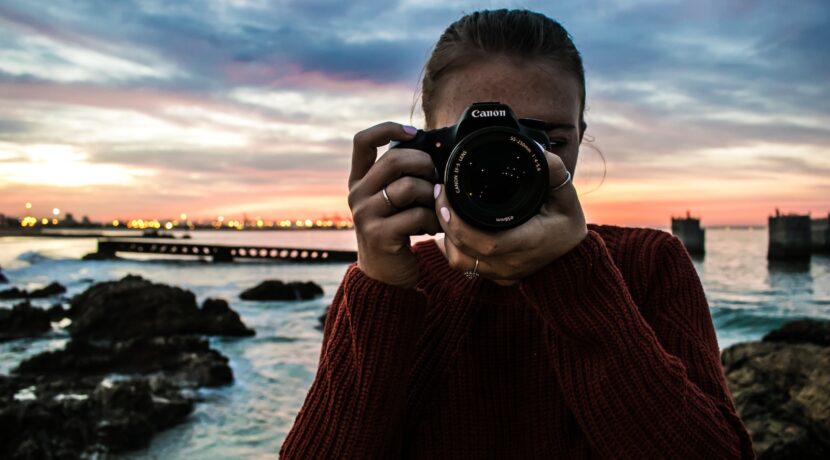 photo of woman holding black Canon DSLR camera near body of water