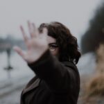 woman in black coat standing near body of water during daytime