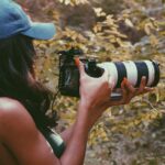 woman in blue cap holding black and white dslr camera
