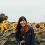 smiling woman standing beside sunflowers