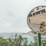 woman in black tank top taking photo of brown concrete building near body of water during