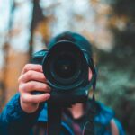 selective focus photography of man holding black DSLR camera