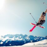 person in brown jacket doing snow ski blade trick