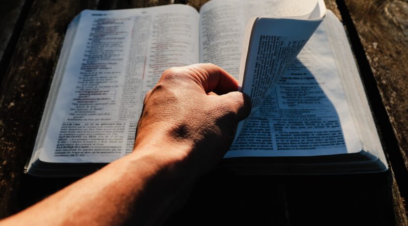 a person holding an open book on top of a wooden table