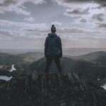man in black jacket standing on rock formation under cloudy sky during daytime