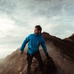 man in blue jacket standing on cliff