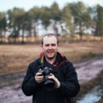 man holding black Nikon DLSR camera while standing on road during daytime