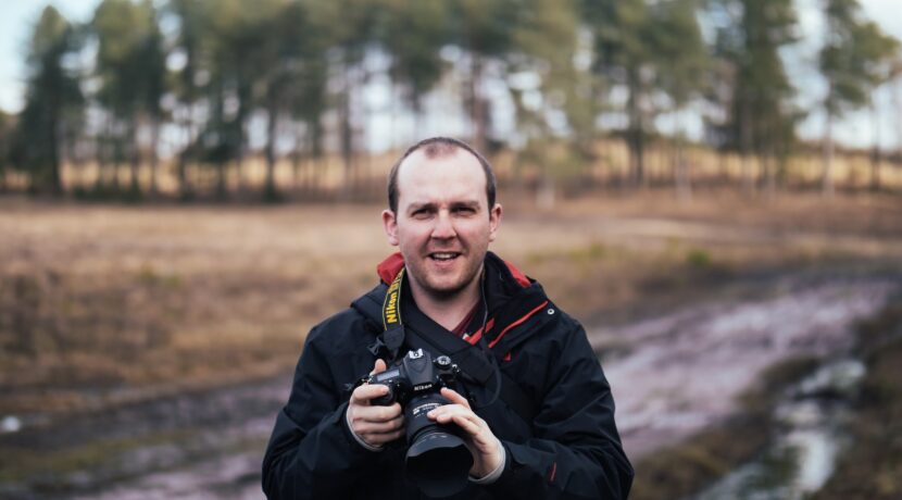 man holding black Nikon DLSR camera while standing on road during daytime