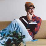 man sitting on sofa while holding book