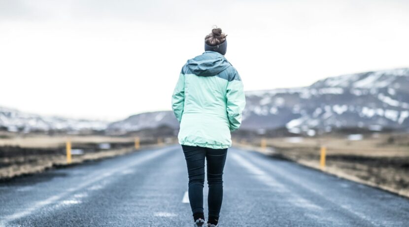 woman wearing teal jacket and black pants walking on concrete road
