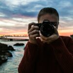 photo of woman holding black Canon DSLR camera near body of water