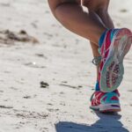 woman in white red and blue sneakers sitting on white sand during daytime