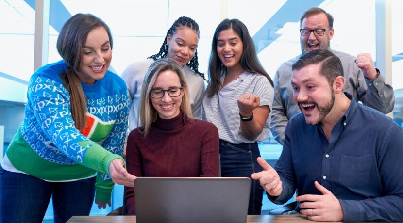 men and women sitting and standing while staring at laptop