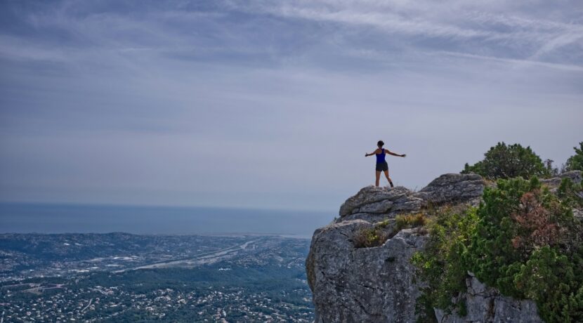 woman standing on cliff overlooking city during daytime