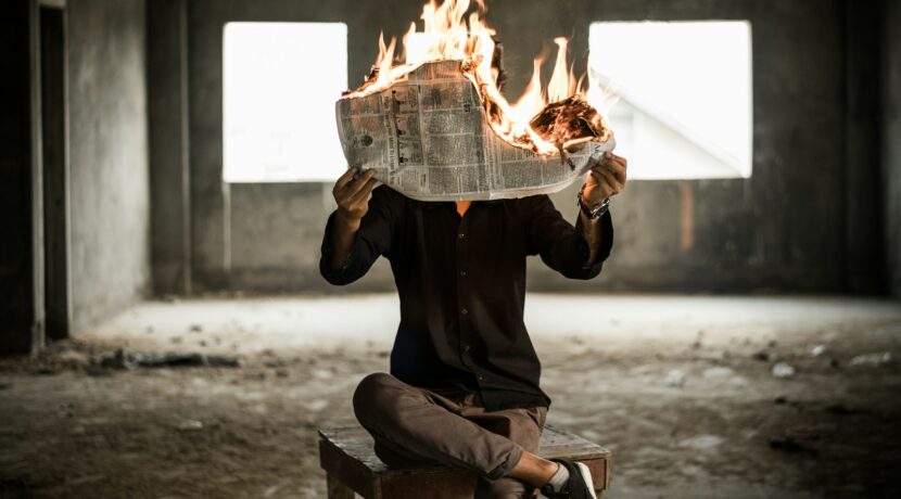 man sitting on chair holding newspaper on fire