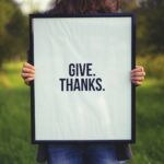 person holding rectangular black wooden photo frame with Give. Thanks. print