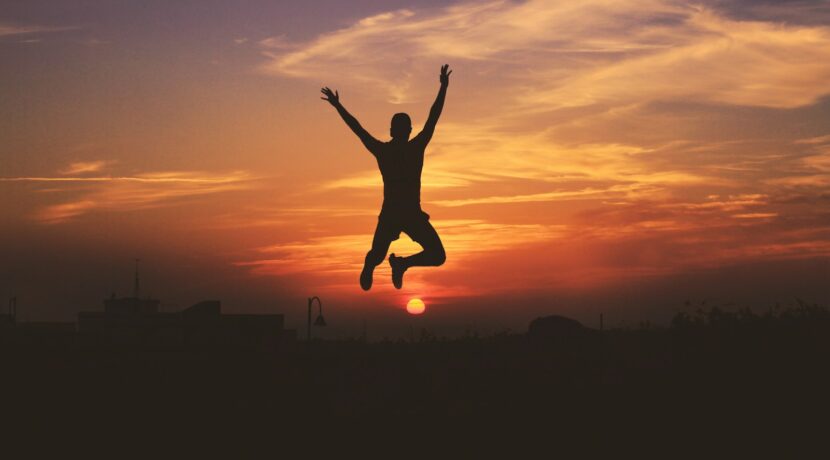 silhouette of man jumping raising both hands during golden hour