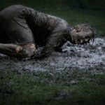 man lying on green grass soaked with mud