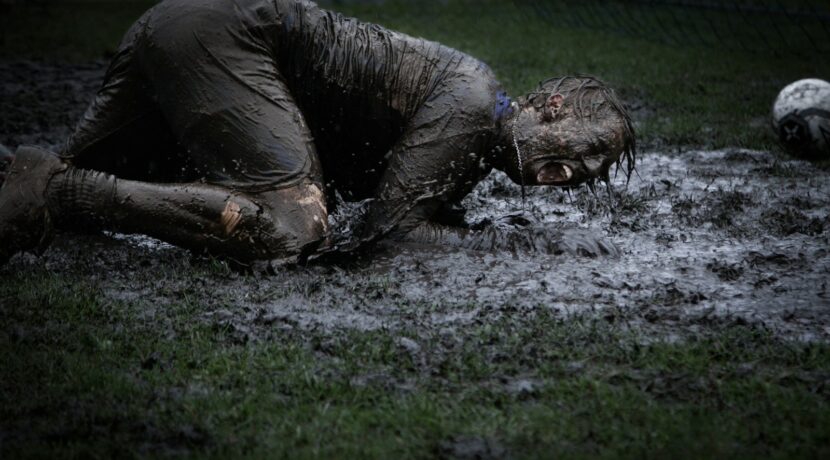man lying on green grass soaked with mud