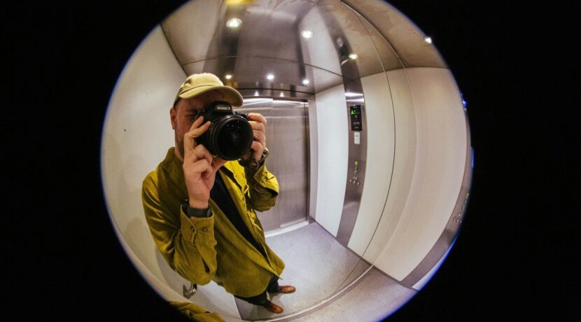 Man in yellow jacket takes selfie in elevator